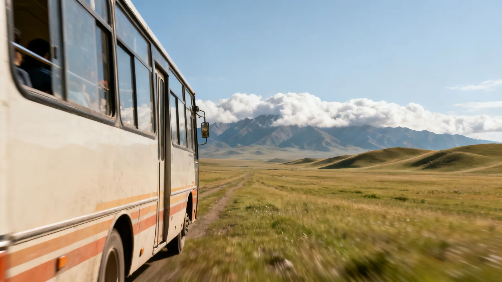 A bus passing through open southern steppe toward distant clouded mountains